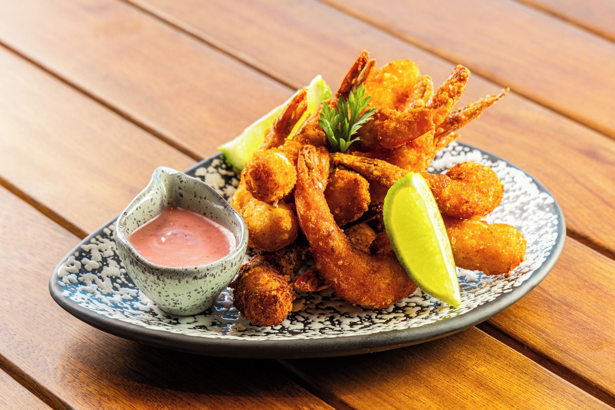 Un plato de camarones fritos con gajos de limón y un recipiente pequeño con salsa para mojar.