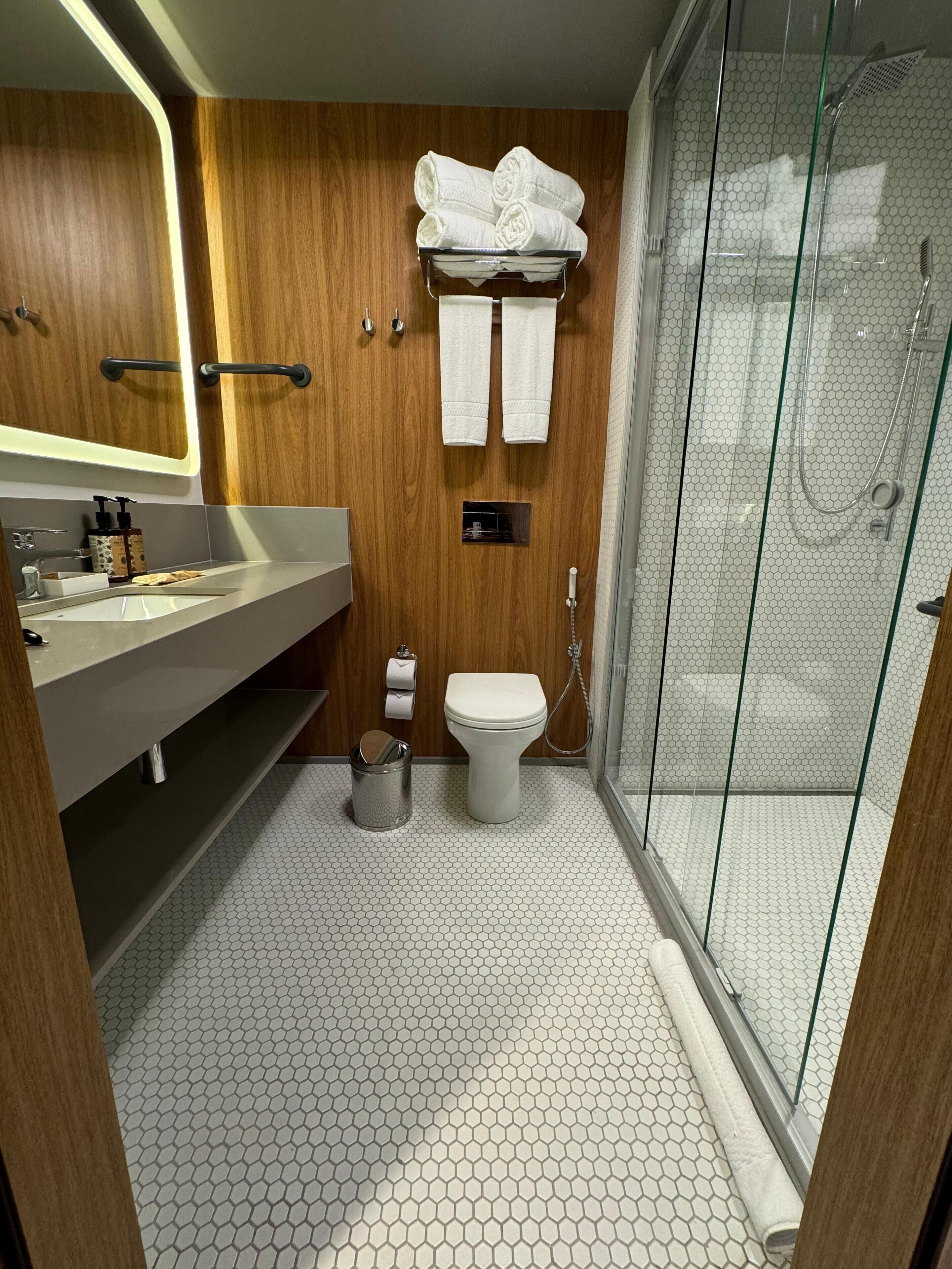 Un baño moderno con tocador de madera, inodoro y cabina de ducha con paredes de vidrio.