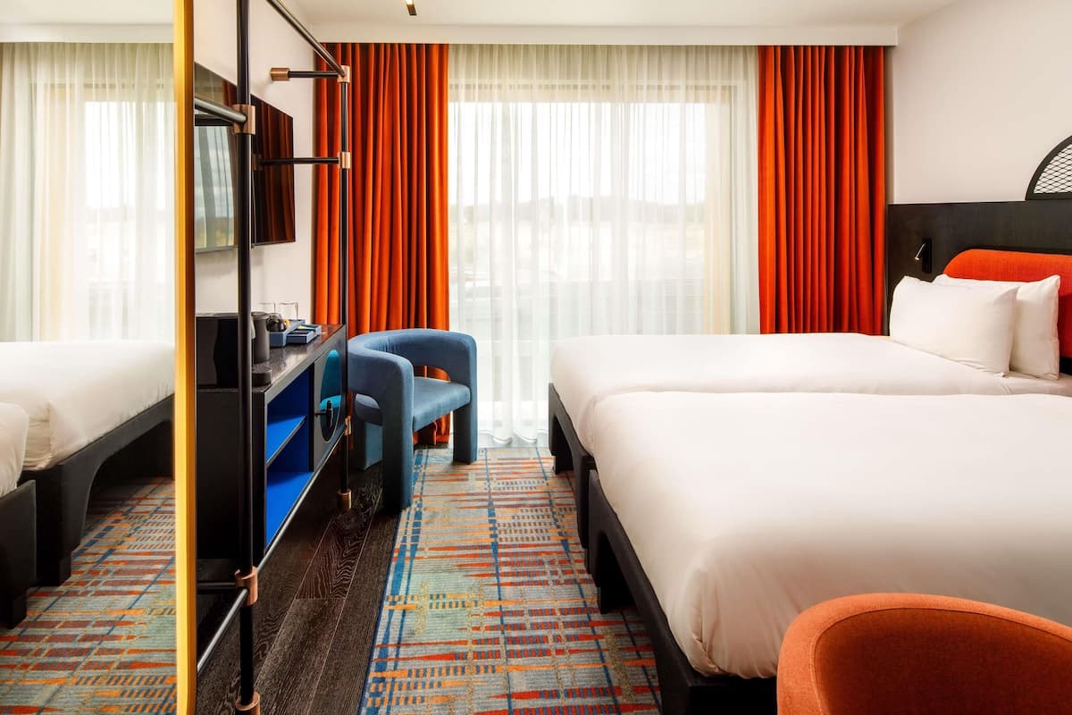 Habitación de hotel con dos camas, un escritorio, una silla y un ventanal con cortinas.