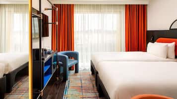 A hotel room with two beds, a desk, a chair, and a large window with curtains.