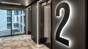 A modern elevator with a large illuminated number "2" on the wall, a patterned carpet, and a view of a building through glass doors. - TRIBE Manchester Airport (Manchester)