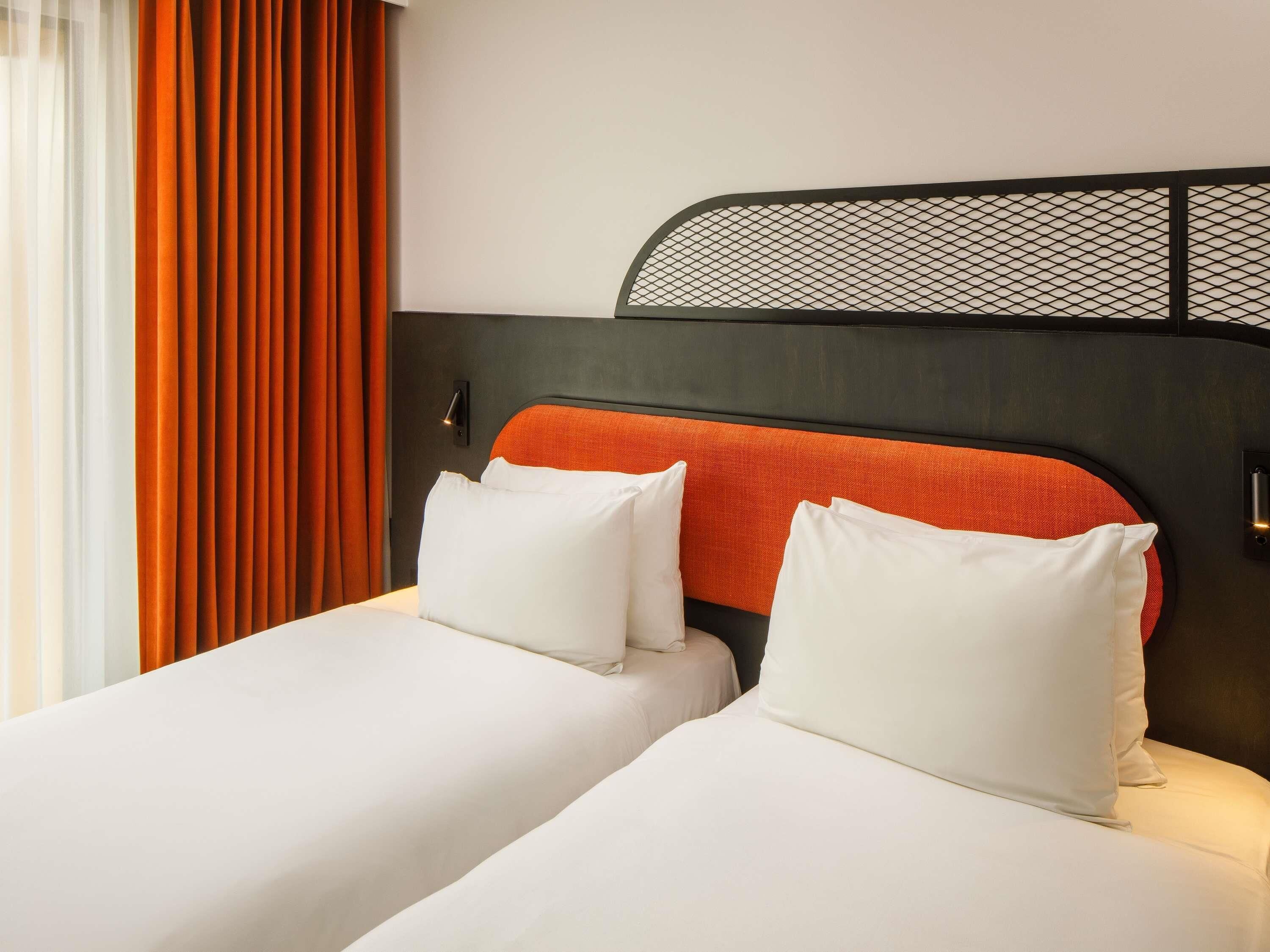 A hotel room with two beds, a headboard with a mesh design, and a window with curtains.