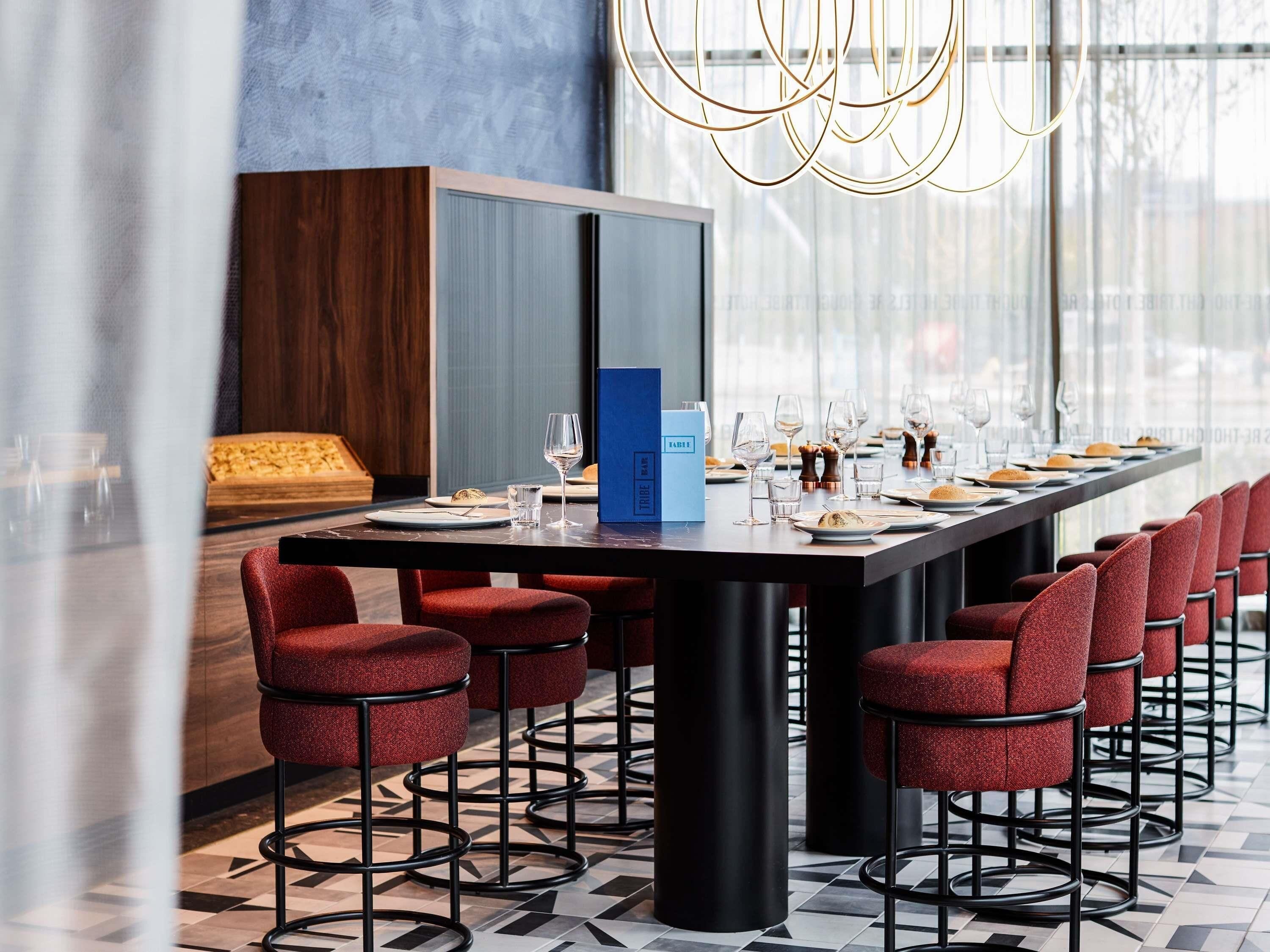 Un comedor moderno con una mesa larga dispuesta para una comida, taburetes de bar tapizados en rojo y un gran ventanal que proporciona luz natural.