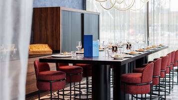 Un comedor moderno con una mesa larga dispuesta para una comida, taburetes de bar tapizados en rojo y un gran ventanal que proporciona luz natural.