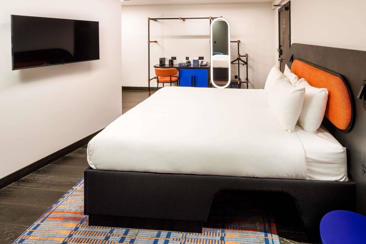 Habitación de hotel con una cama grande, un televisor de pantalla plana en la pared, un escritorio con una silla y un espejo.