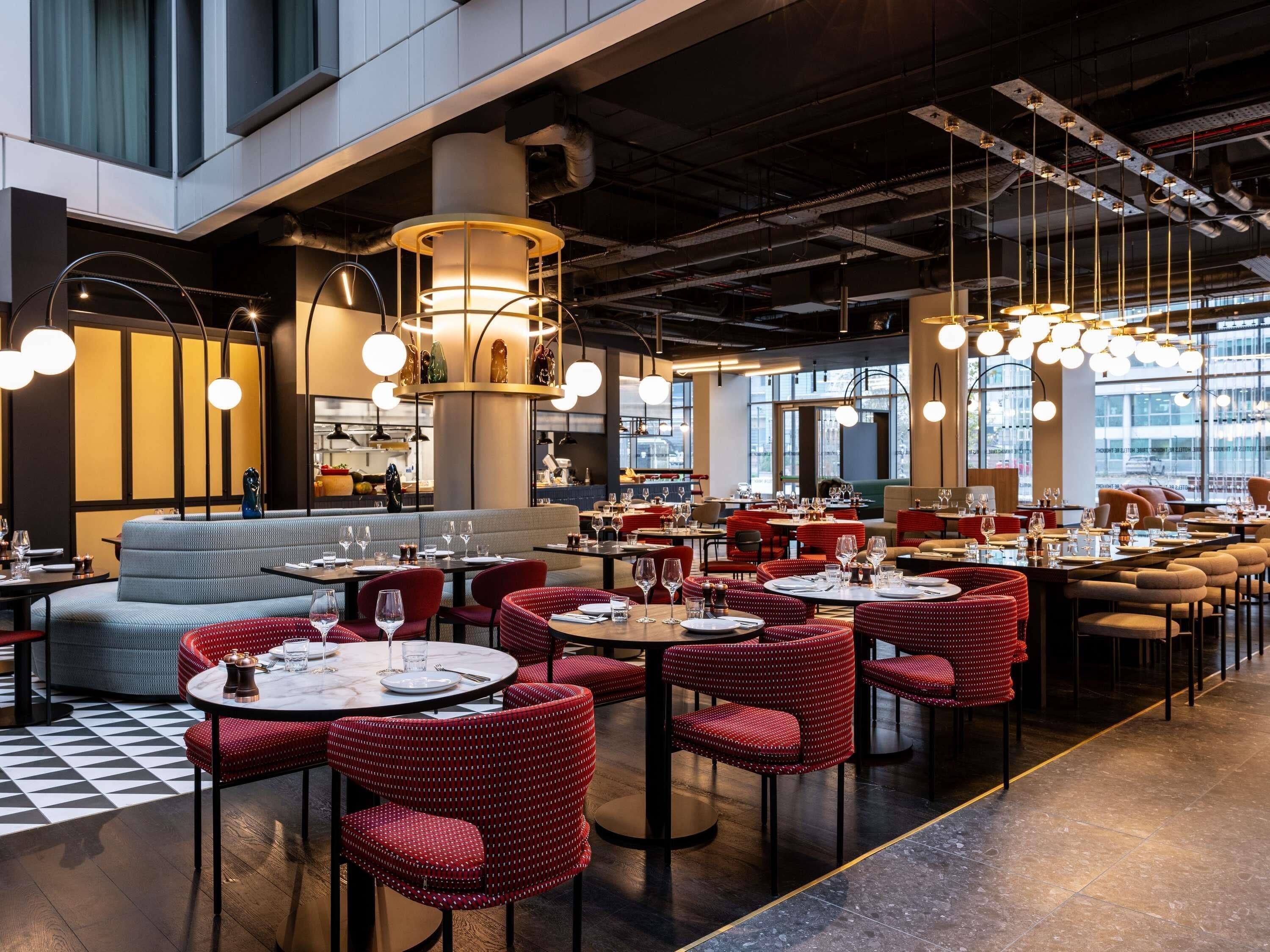 A modern restaurant interior with round tables, red upholstered chairs, and pendant lighting.