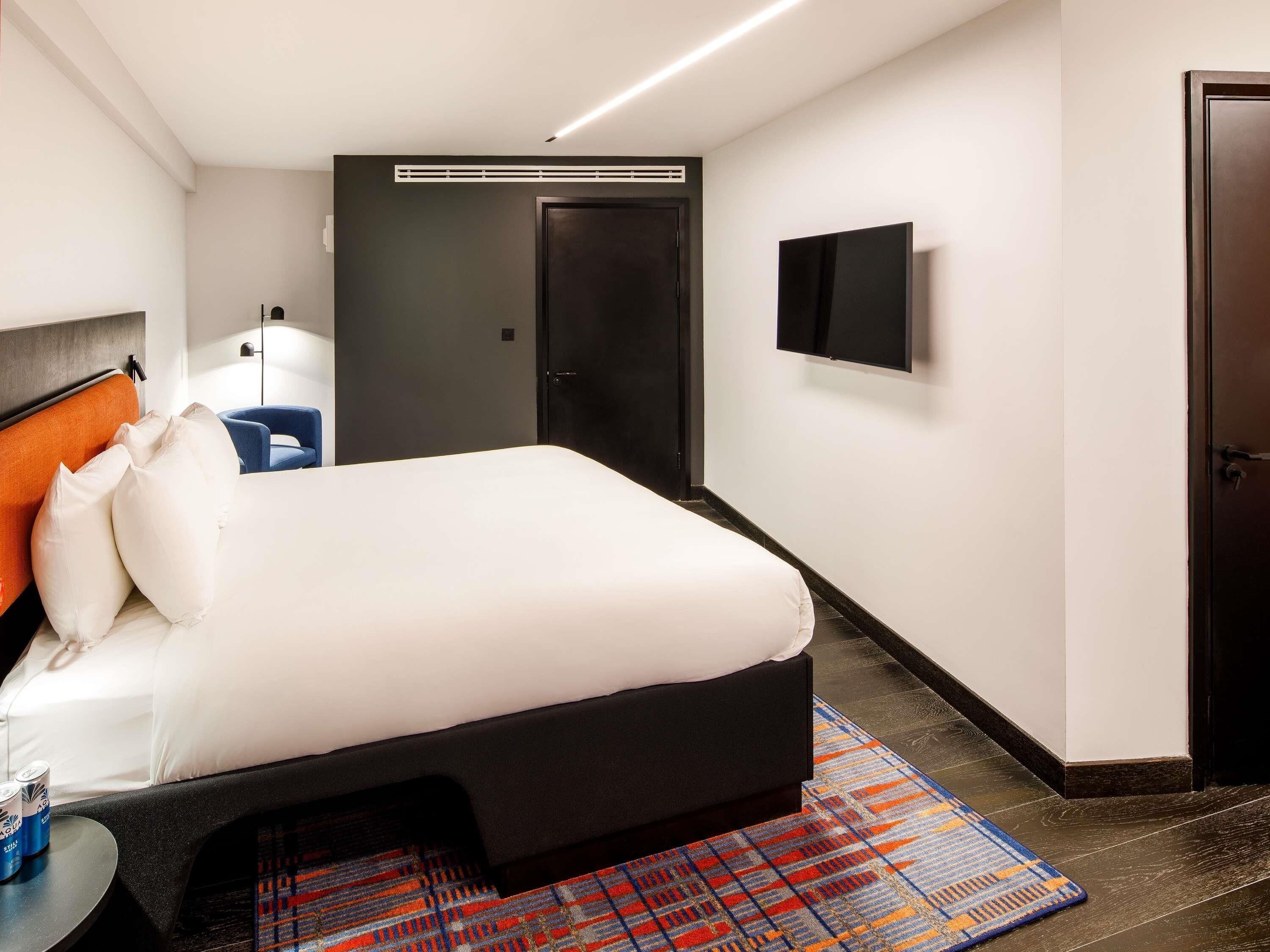 Una habitación de hotel moderna con una cama grande, un televisor de pantalla plana, una puerta oscura y una alfombra estampada.