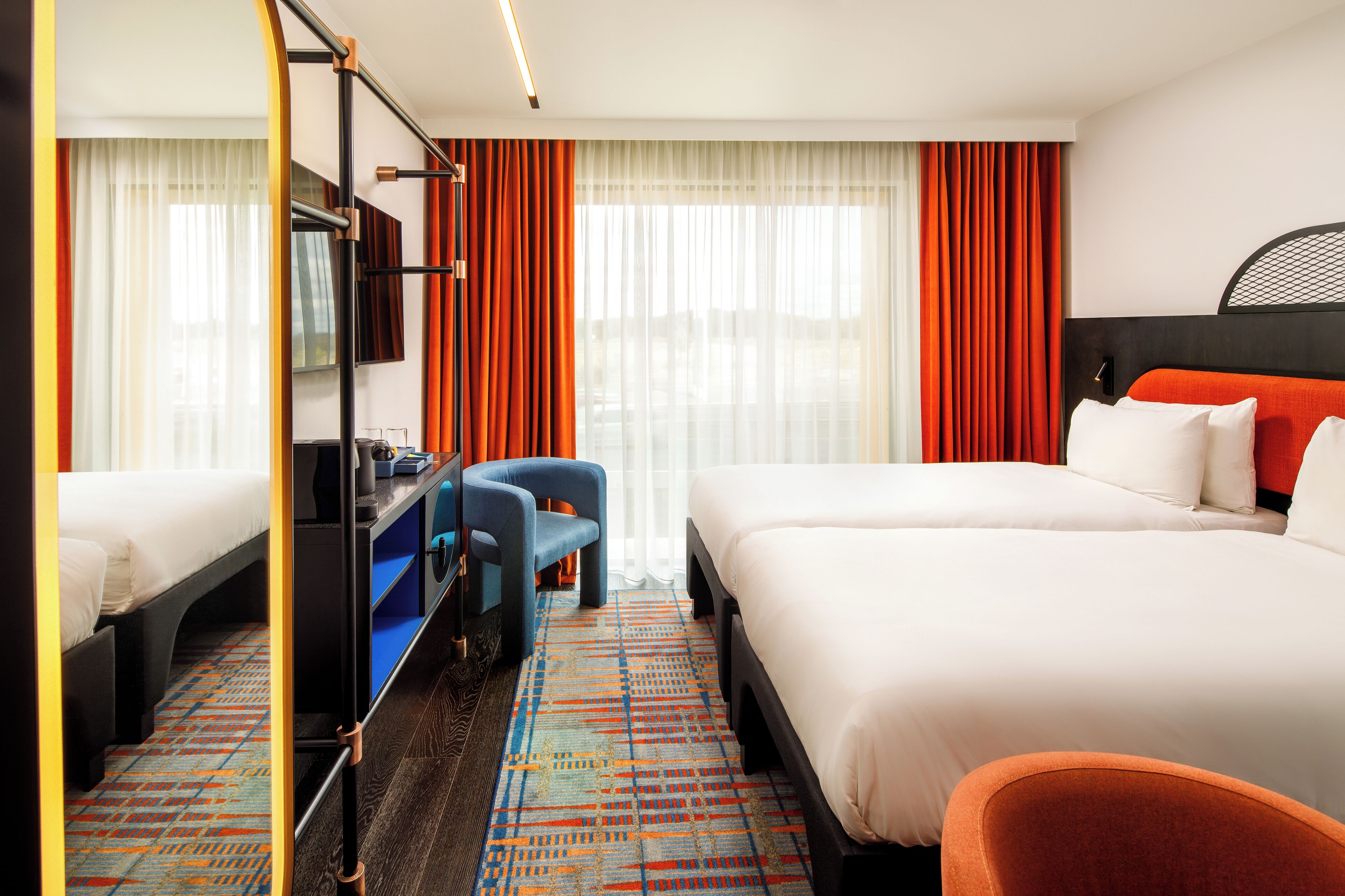A hotel room with two beds, a desk, a chair, and a television.