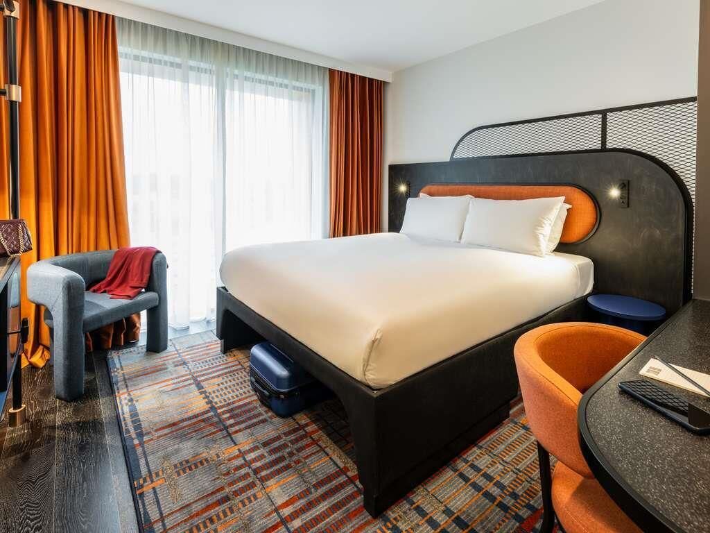 A hotel room with a large bed, a desk, a chair, and a patterned rug.