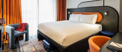 A hotel room with a large bed, a desk, a chair, and a patterned rug.