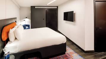 Ein modernes Hotelzimmer mit einem großen Bett, einem Flachbildfernseher, einer dunklen Tür und einem kleinen Tisch mit einer Flasche und Dosen.
