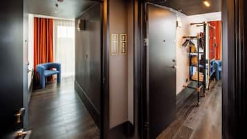 A hotel hallway with dark wooden floors, a blue chair, and a coat rack with hanging items.
