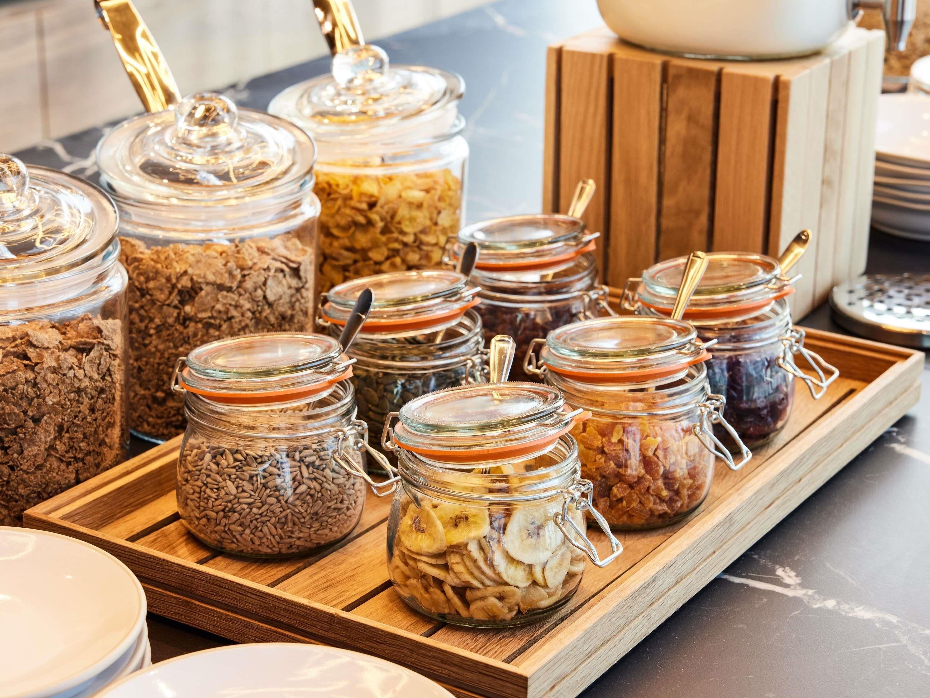 A buffet with various food items in glass jars on a wooden tray.