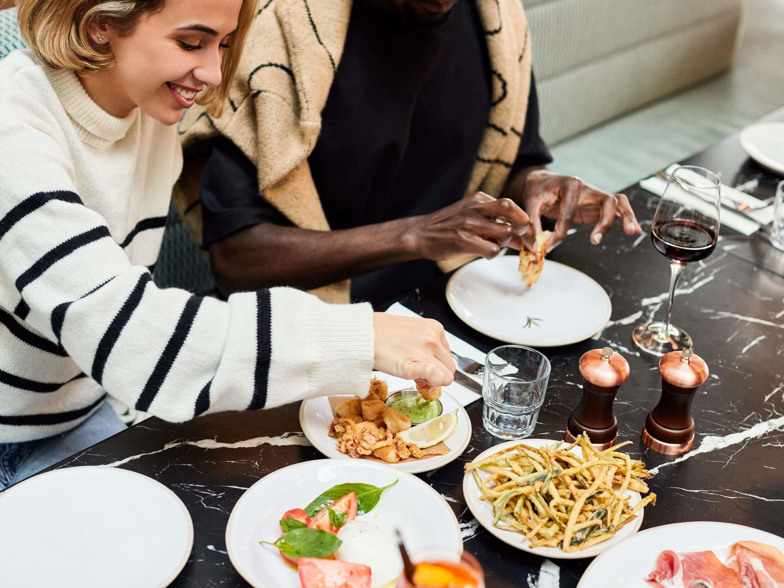 A dining table with plates of food, a glass of red wine, and two salt shakers.