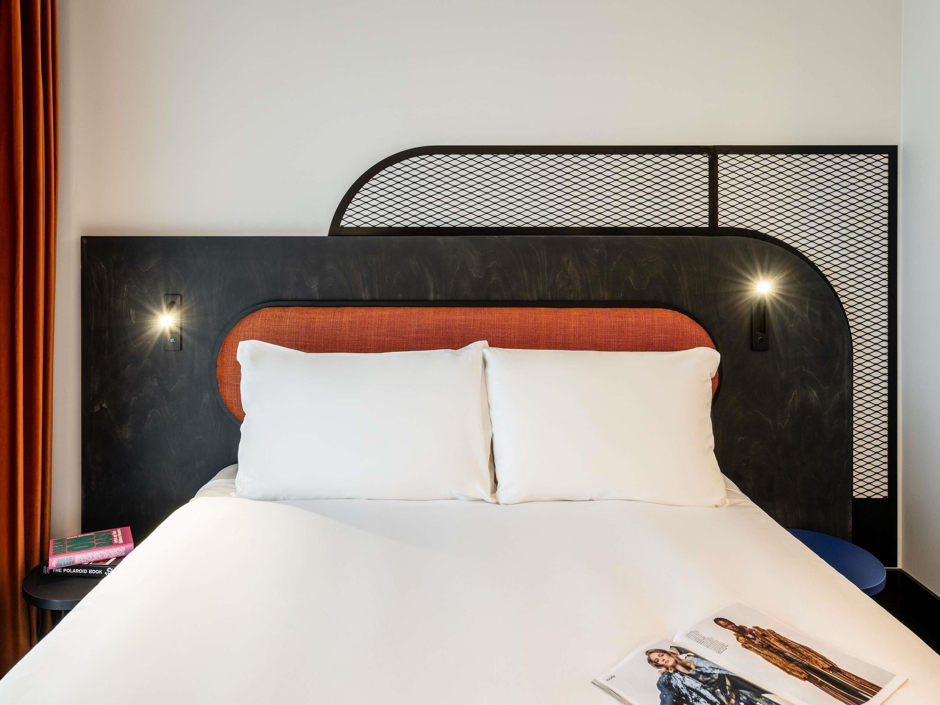 A bed with white bedding, a black headboard with a geometric pattern, and two wall-mounted lights.