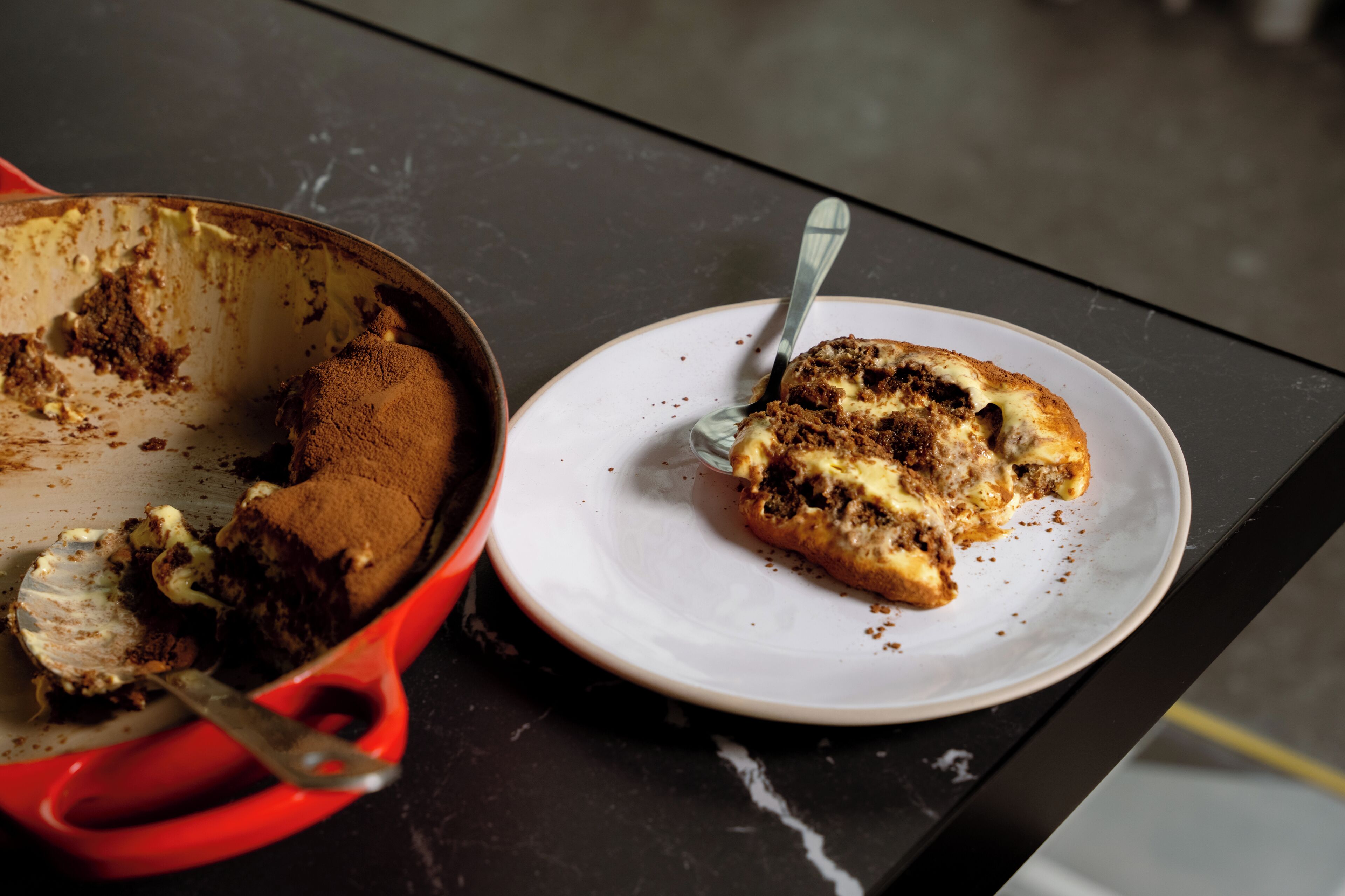 A partially eaten dessert in a red pan and a plate with a spoon on a table.