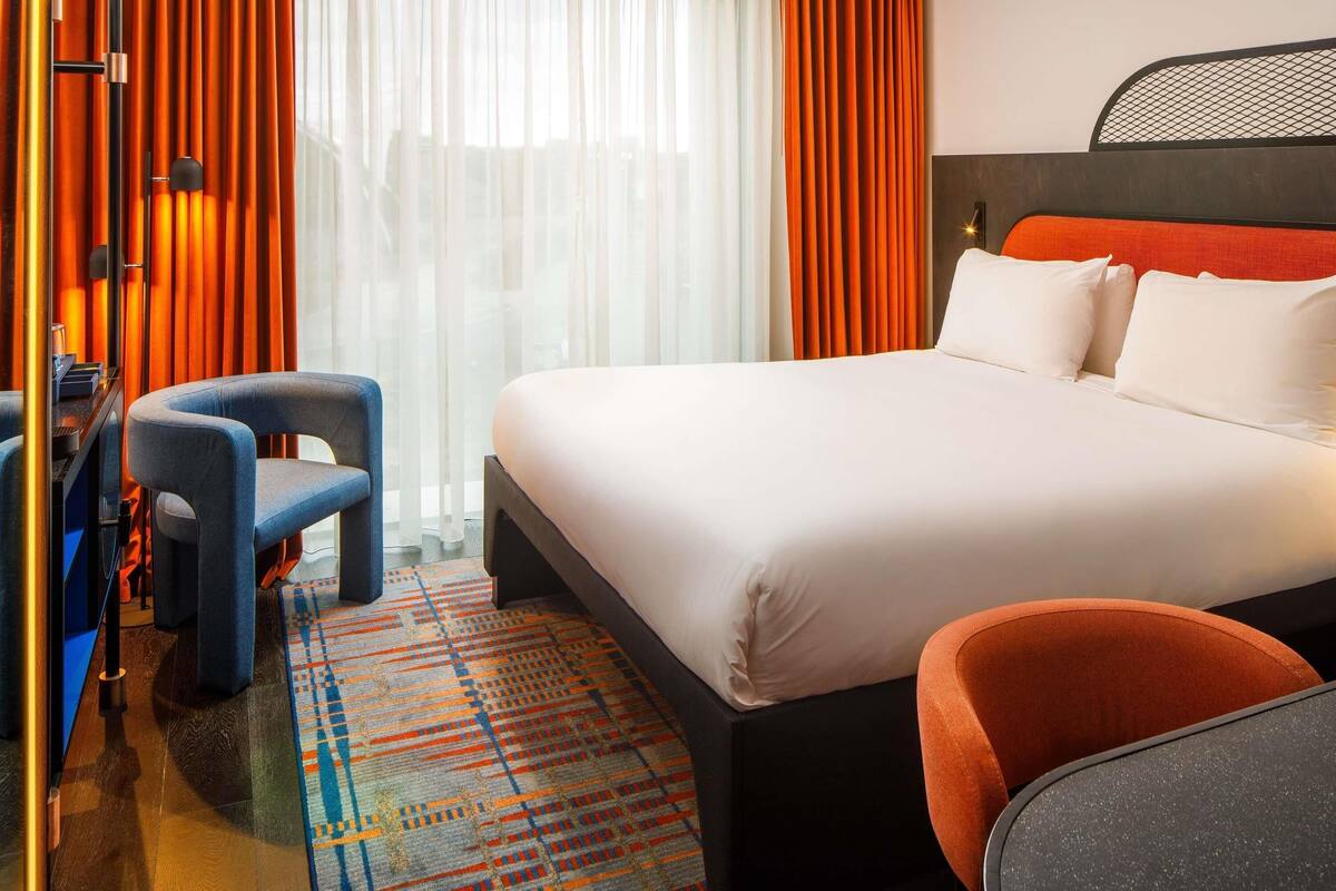 A hotel room with a bed, two chairs, a desk, and a patterned rug.