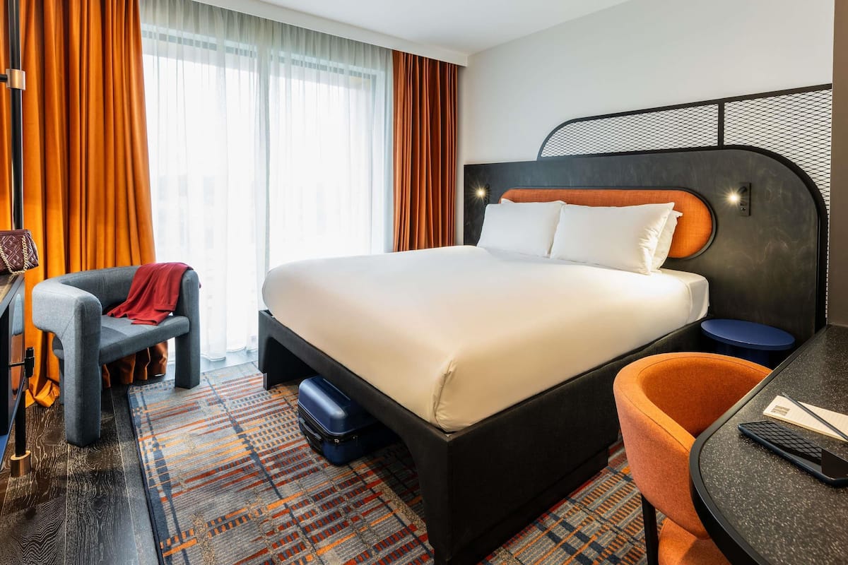 A modern hotel room with a large bed, a desk, and a chair.