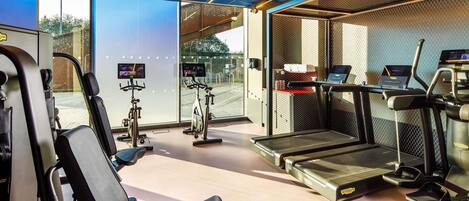 Un gimnasio moderno con equipamiento de ejercicio, incluyendo cintas de correr y bicicletas estáticas, y ventanas amplias que ofrecen vistas al exterior.