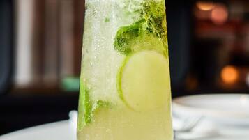 A tall glass with a lime slice and mint leaves, filled with a clear liquid, possibly a cocktail, on a white surface.
