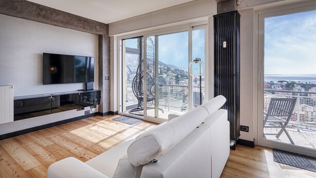 A modern living room with a large TV, a sofa, and a balcony with a city view. - Stunning Seaview Apartment by Wonderful Italy (Genoa)