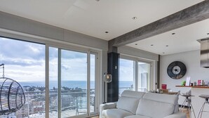 A modern living room with a large window, a sofa, a dining area, and a kitchen. - Stunning Seaview Apartment by Wonderful Italy (Genoa)
