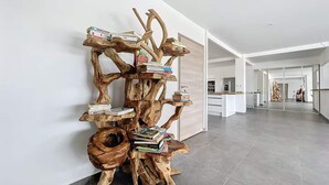 A modern interior with a unique wooden bookshelf structure against a white wall, a kitchen area in the background, and a spacious hallway. - Lodge Wanalao - 4 rooms (Sainte-Anne)