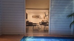 A swimming pool with a wooden deck, a dining area with chairs and a table, and a living room with a sofa and a coffee table. - Lodge Wanalao - 4 rooms (Sainte-Anne)