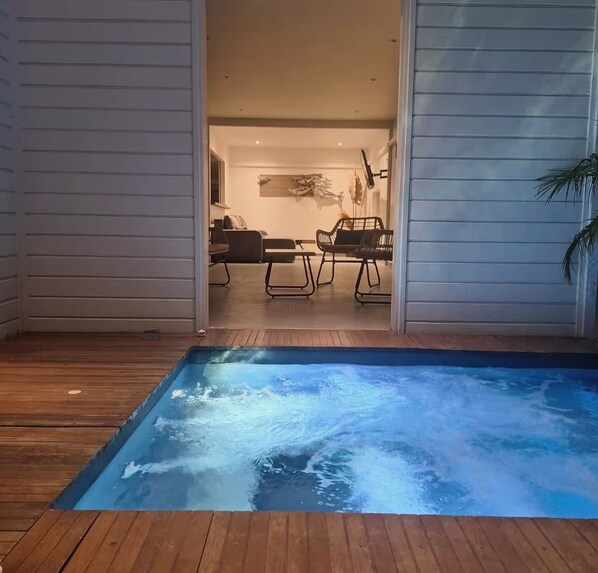 Una piscina con cubierta de madera, un comedor con sillas y mesa, y una sala de estar con sofá y mesita de centro.