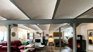 Un salón espacioso con un sofá rojo, un sillón verde y un televisor. Se ve una chimenea y una estantería al fondo.