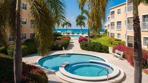Een resort met een centraal gelegen zwembad, palmbomen en uitzicht op de oceaan.