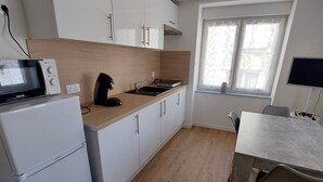 Eine moderne Küche mit weißen Schränken, einer eingebauten Mikrowelle und einer Kaffeemaschine. Ein Esstisch mit Stühlen und ein Fenster mit Vorhängen sind ebenfalls vorhanden.