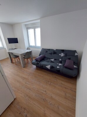 Una sala de estar moderna con un sofá, una mesa de comedor con sillas y un televisor de pantalla plana montado en la pared.