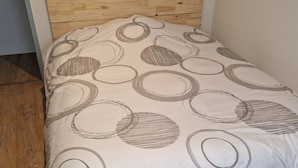 Ein Einzelbett mit hölzernem Kopfteil und weißer Bettdecke mit kreisförmigen Mustern.