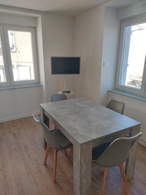 Un comedor moderno con una mesa rectangular, cuatro sillas, un televisor de pantalla plana montado en la pared y ventanas amplias que ofrecen luz natural.