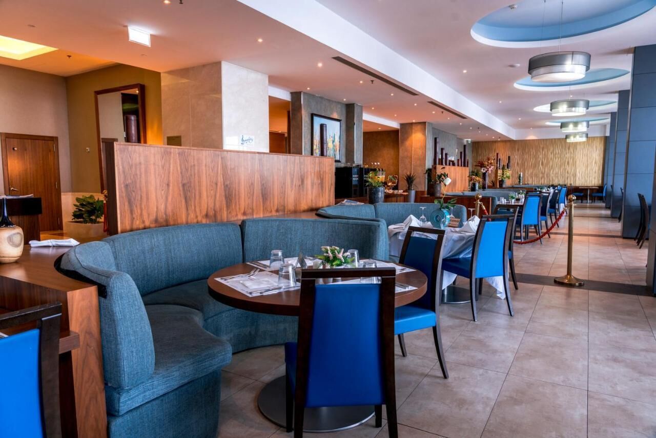 A modern hotel lobby with a reception desk, seating areas, and a dining section.
