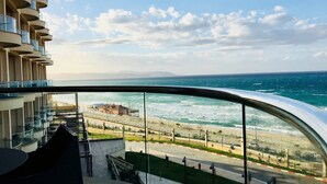 A high-rise building with a curved glass balcony overlooking a beach and ocean. - Royal Tulip Skikda (Filfila)