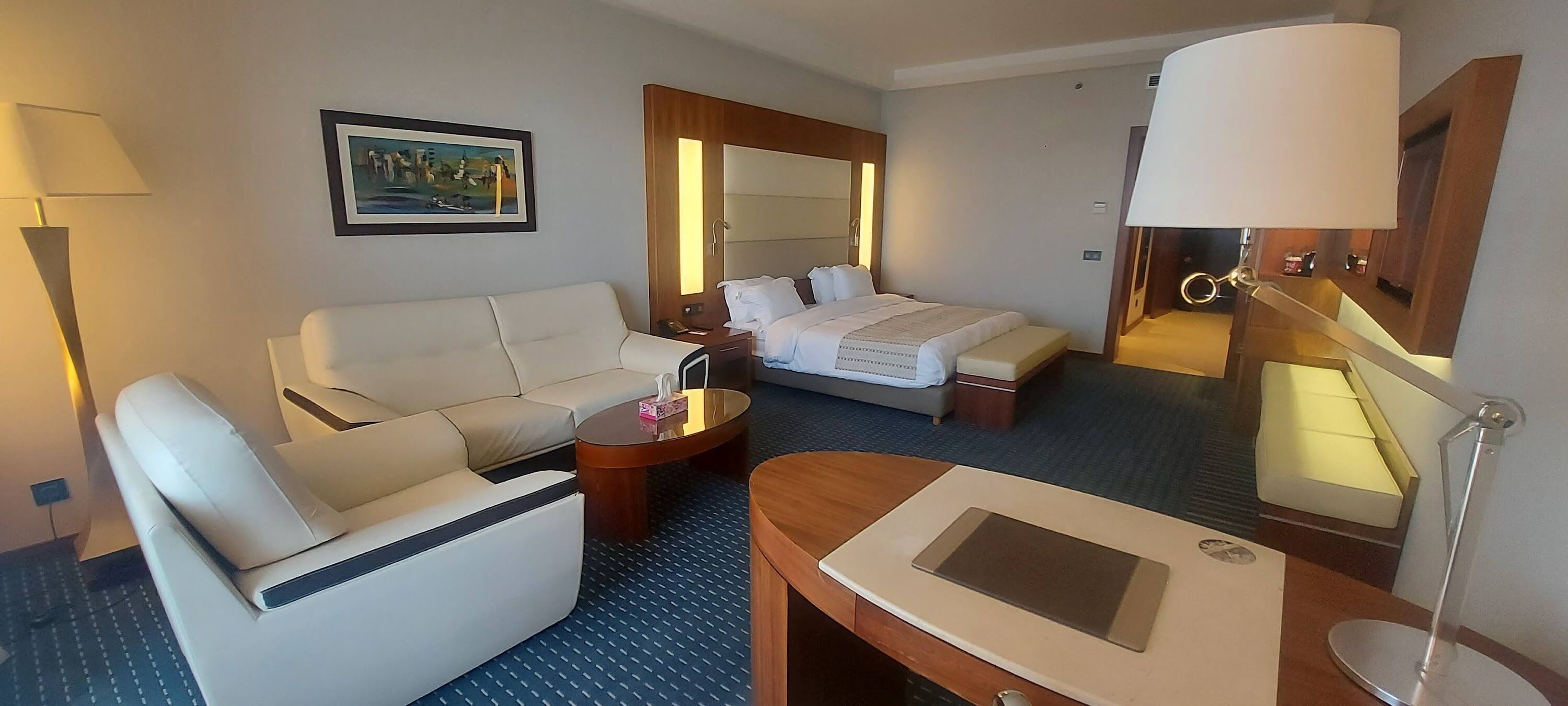 Una camera d'hotel con un letto, una poltrona, una scrivania, una lampada e un quadro appeso al muro.