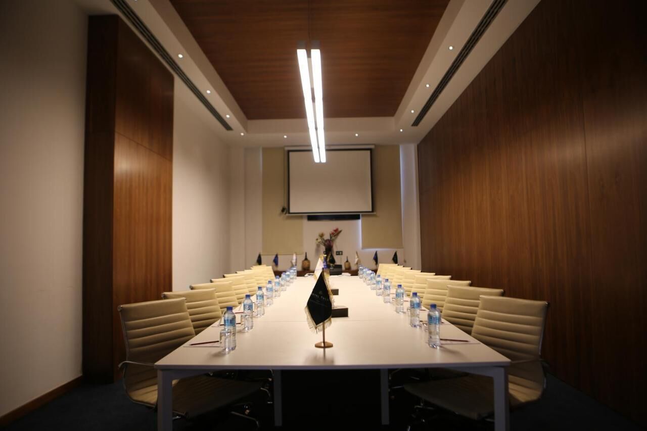 Un salón de conferencias con una larga mesa, sillas, botellas de agua y una pantalla de proyector.