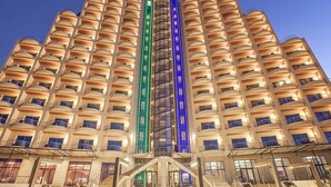 A high-rise hotel with multiple balconies, a central glass elevator shaft, and a symmetrical facade. - Royal Tulip Skikda (Filfila)