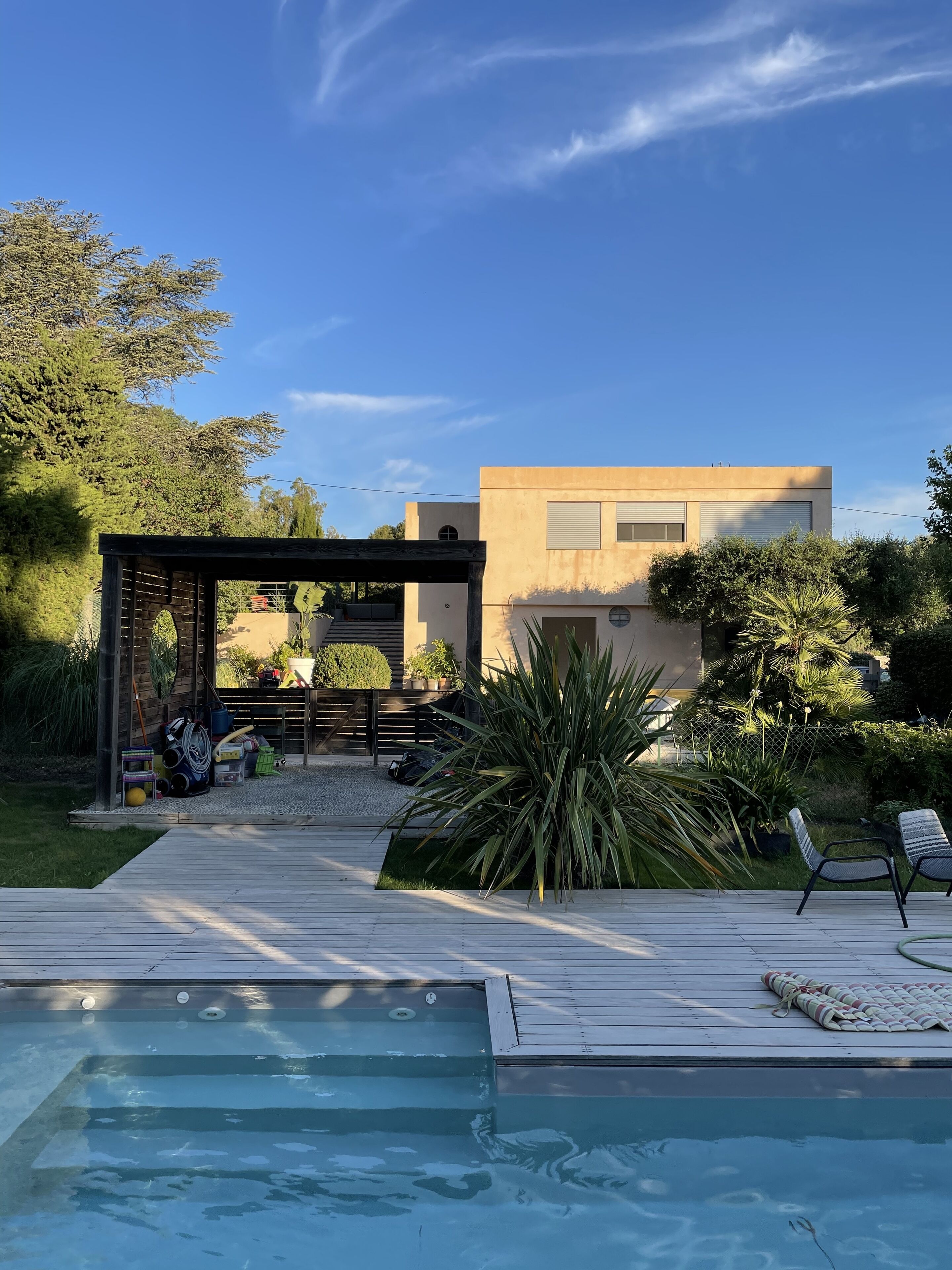 Ett modernt utomhuspoolområde med ett trädäck, solstolar och en pergola.