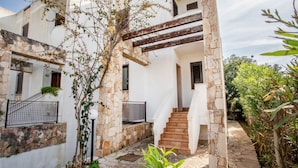 Um edifício revestido de pedra com uma escadaria que leva a um andar superior, cercado por vegetação.