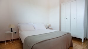 Quarto com cama, duas mesas de cabeceira, guarda-roupa e piso de madeira.