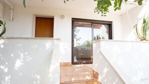 Área externa moderna com porta de madeira, porta de correr de vidro que dá para um pátio e piso ladrilhado.
