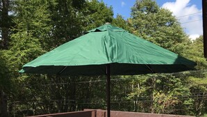 A round table with a green umbrella, surrounded by four white plastic chairs, set on a concrete deck with a wooden railing. - New togakushi schiheil (Nagano)