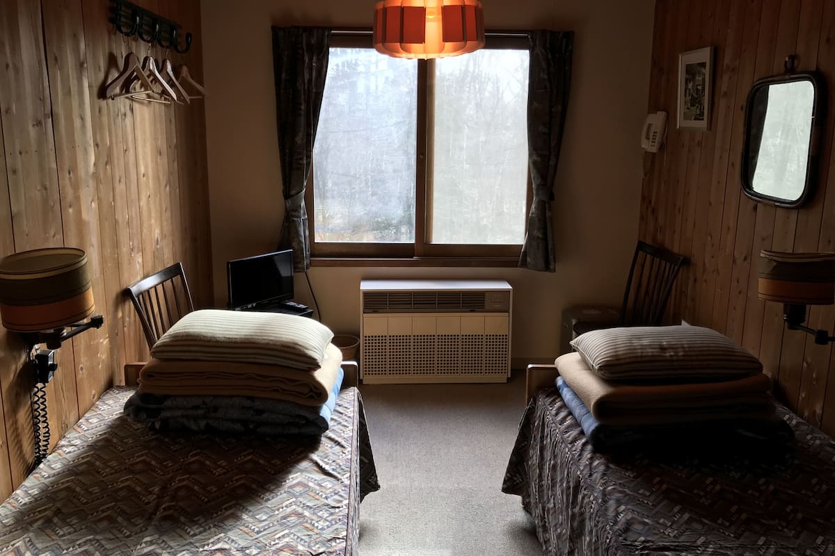 A room with two beds, a heater, a window with curtains, a telephone, and a mirror.