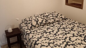 Una camera da letto con un letto, un comodino con una lampada, uno specchio e una piccola finestra.