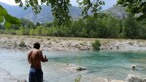 Una persona in piedi vicino a un fiume limpido con sponde rocciose e vegetazione sullo sfondo.