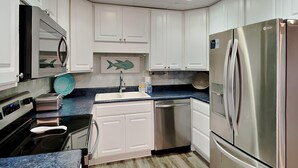 Una cocina moderna con armarios blancos, un refrigerador de acero inoxidable, un lavavajillas y un microondas.