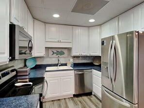 A modern kitchen with white cabinets, a stainless steel refrigerator, a dishwasher, and a microwave.